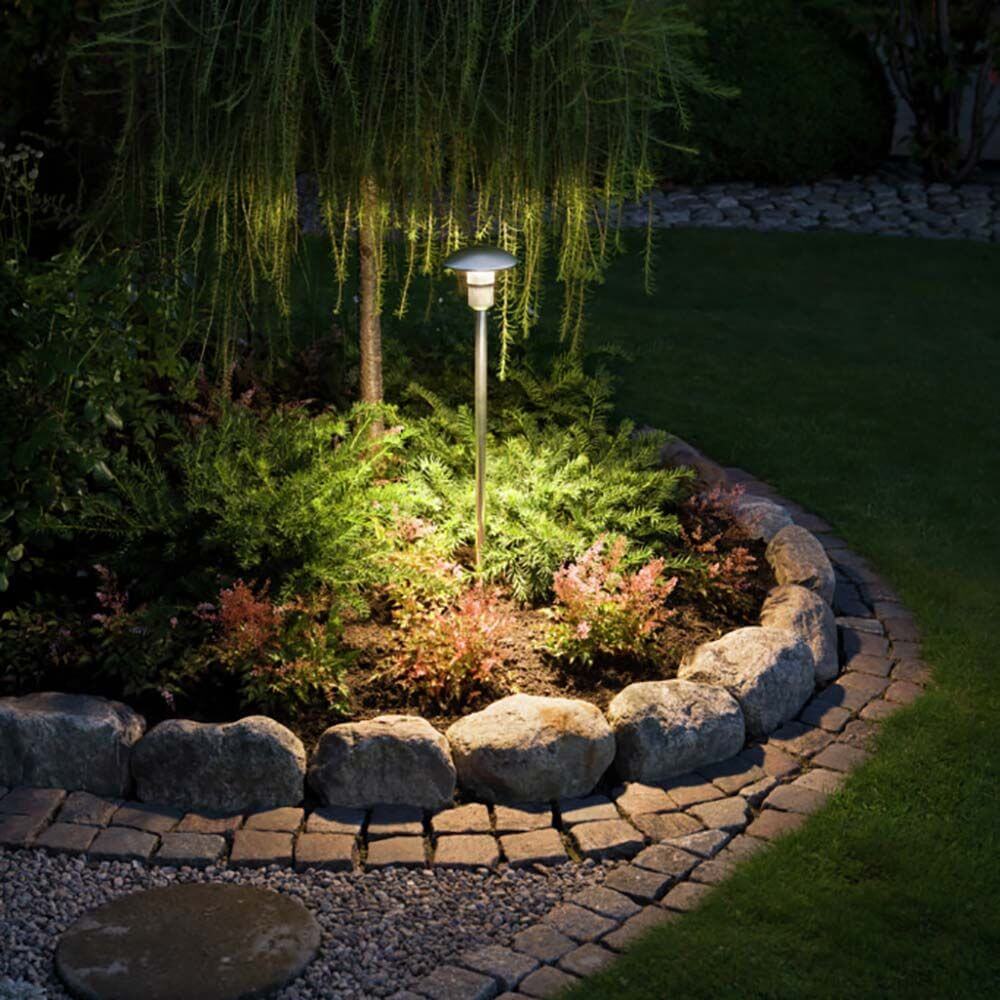Top Cap Reflektor für Monza Erdspießleuchte beleuchtet Gartenbereich mit Pflanzen und Steinen.