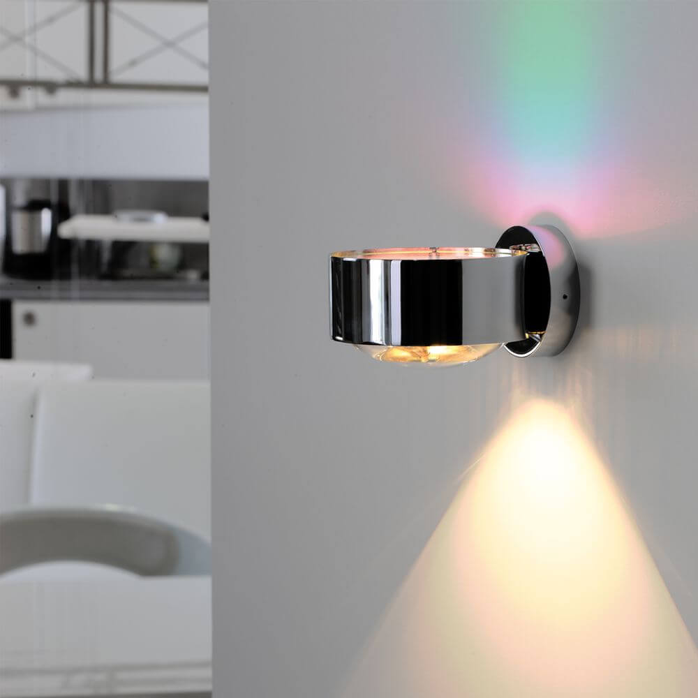 LED Wandleuchte Puk Maxx Wall Dimmbar an einer Wand installiert, modernes und klares Design mit RGB-Lichtakzent.