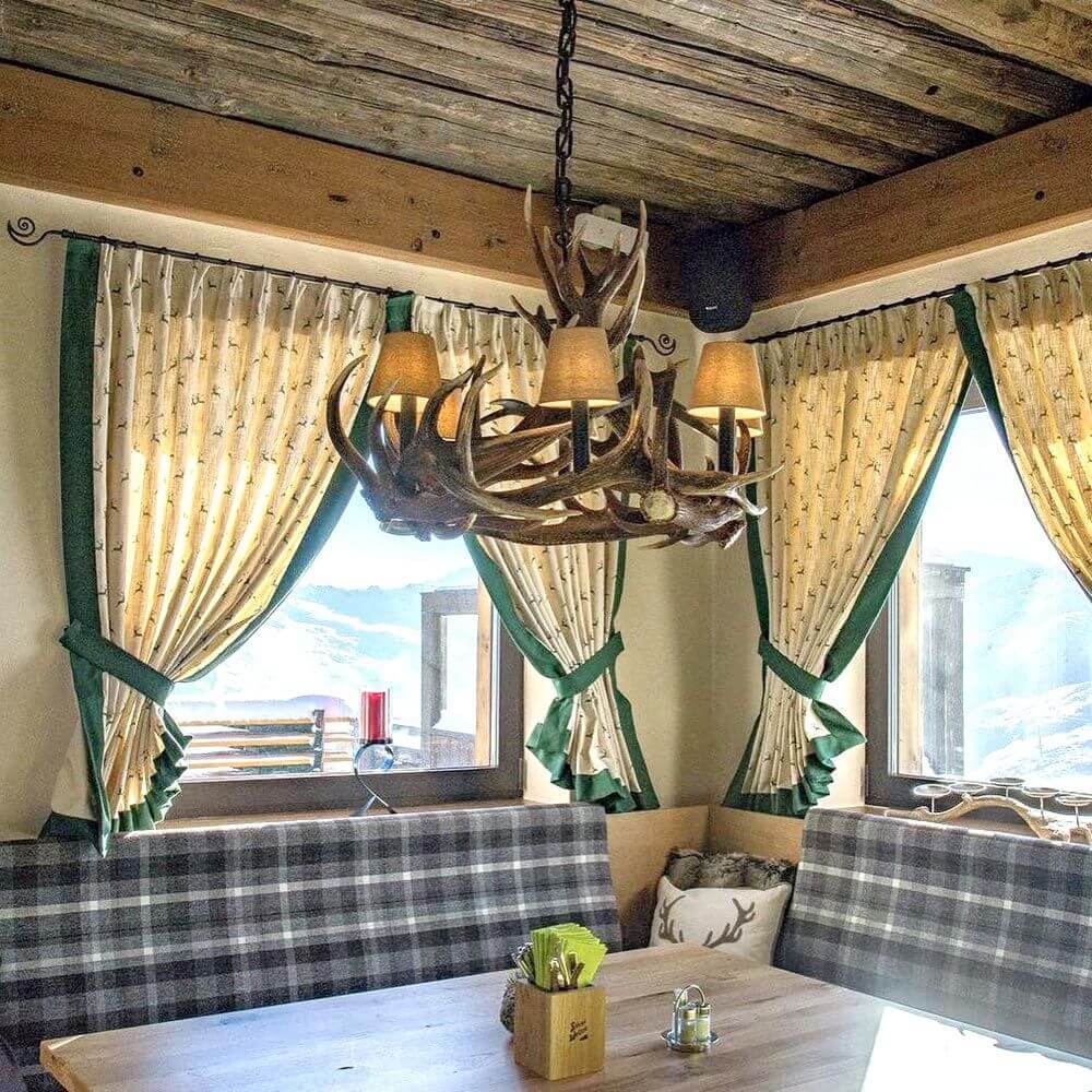 Traditioneller Geweih Kronleuchter Ø 80cm für Chalet in gemütlichem Esszimmer mit Fensterdekoration.