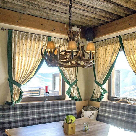 Traditioneller Geweih Kronleuchter Ø 80cm für Chalet in gemütlichem Esszimmer mit Fensterdekoration.