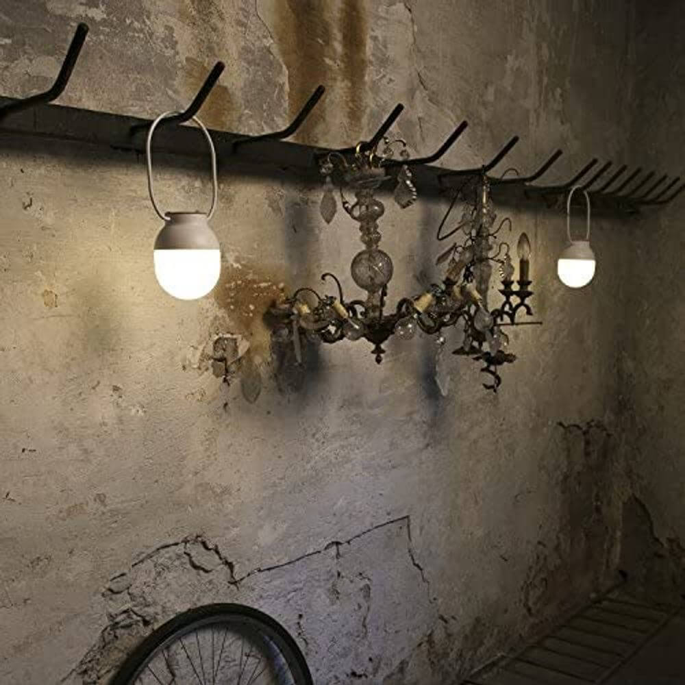 Tragbare Lampe TAKE AWAY Weiß Akku hängt an einem Metallhaken in einem rustikalen Raum.
