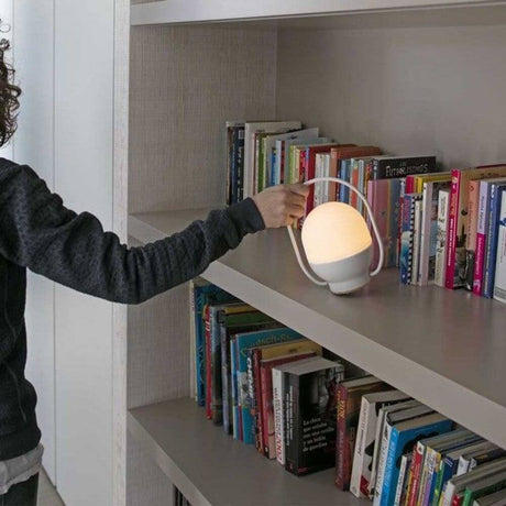 Tragbare Leuchte TAKE AWAY Schwarz, Weiß Akkuleuchte auf einem Regal mit Bücher. Hand greift die Lampe.
