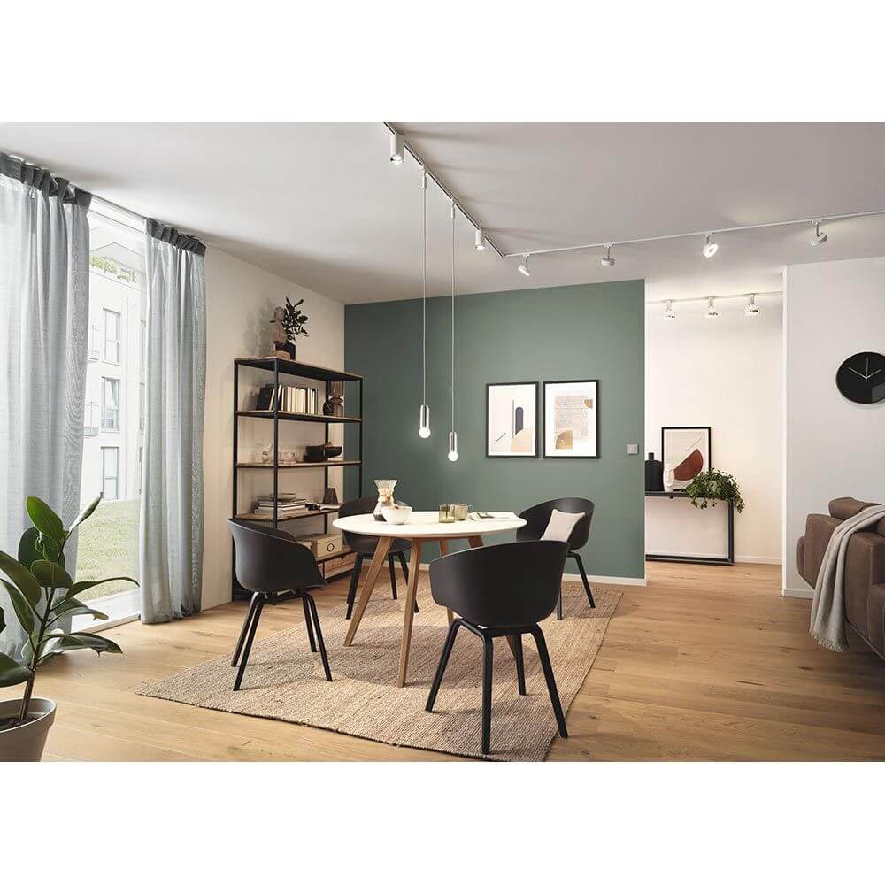 Heller Essbereich mit URail Beleuchtung, modernen Stühlen und einem Bücherregal an einer grünen Wand.