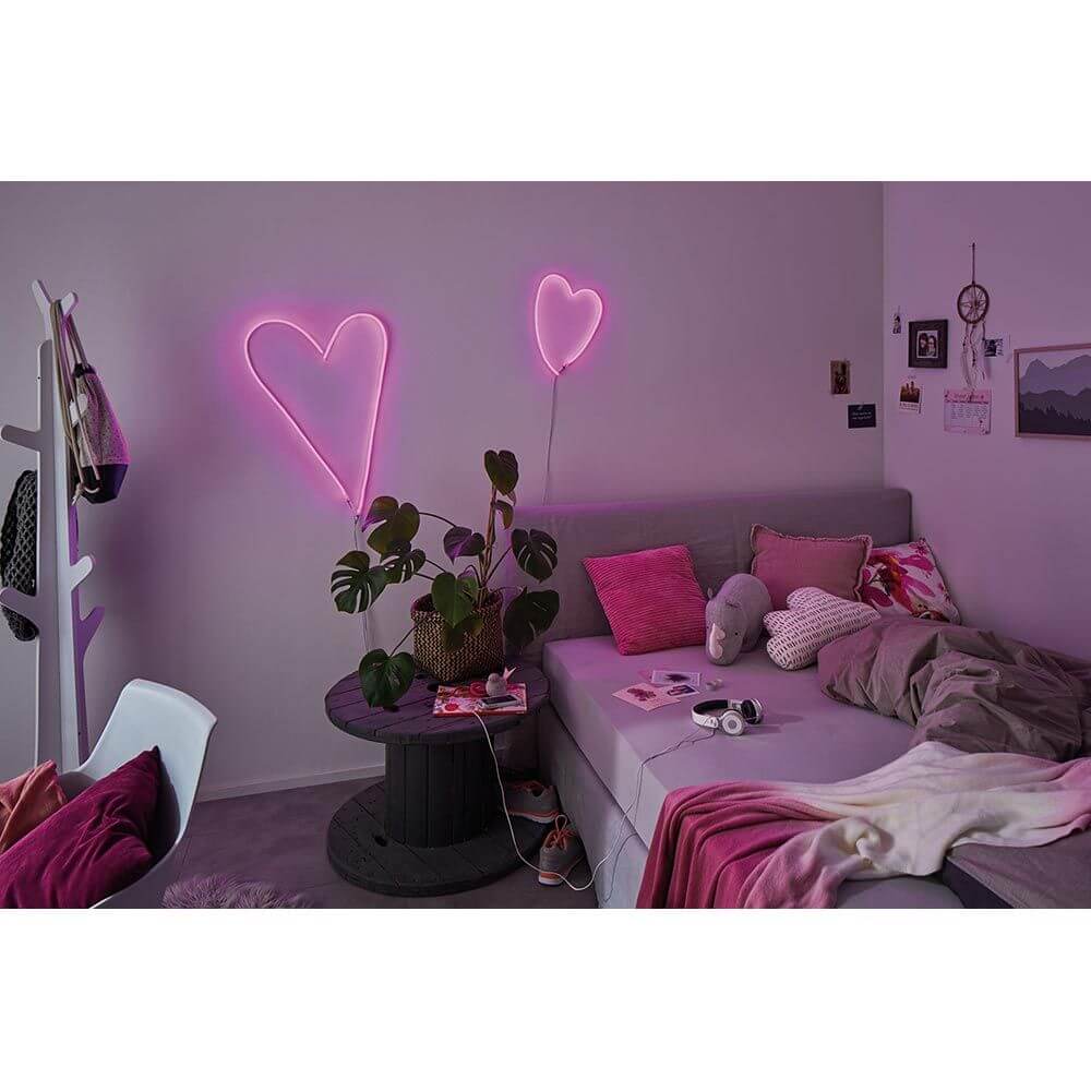 Neonlicht in Herzform in einem gemütlichen Zimmer mit pinkem Dekor und Pflanzen.