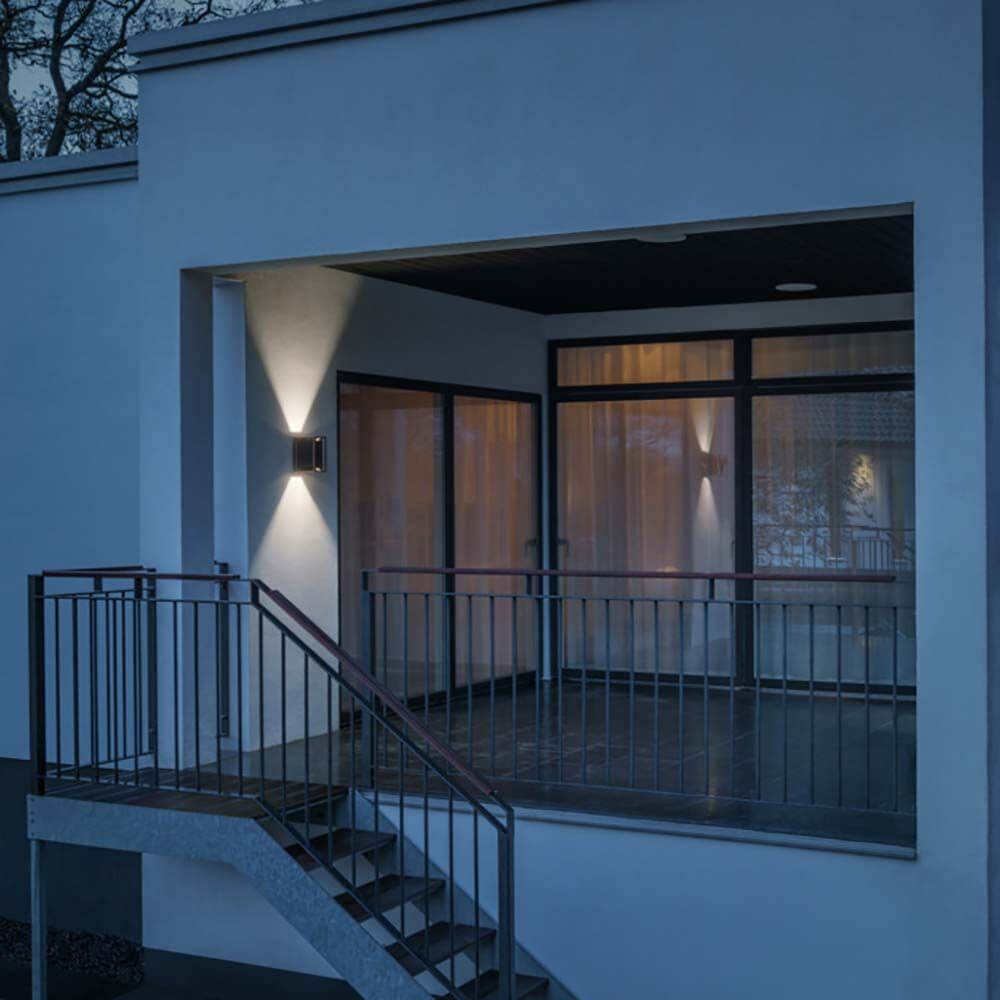 Vale Außenwandleuchte 2-flammig an einer modernen Hauswand im Dunkeln leuchtend.