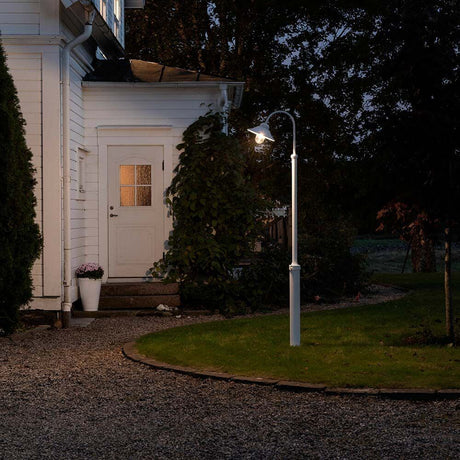 Lampadaire Vega blanc, verre transparent illumine le jardin devant une maison blanche la nuit.