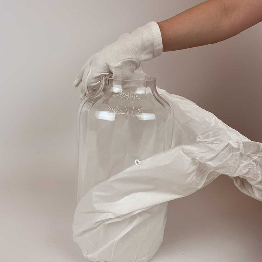 Hand in Handschuh hält einen großen transparenten Behälter mit einer Plastikfolie, perfekte Pflege und Schutz.