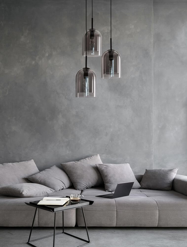 Moderne Hängelampe mit 3 Glaskugeln über einer grauen Couch und Tisch im minimalistischen Wohnzimmer.