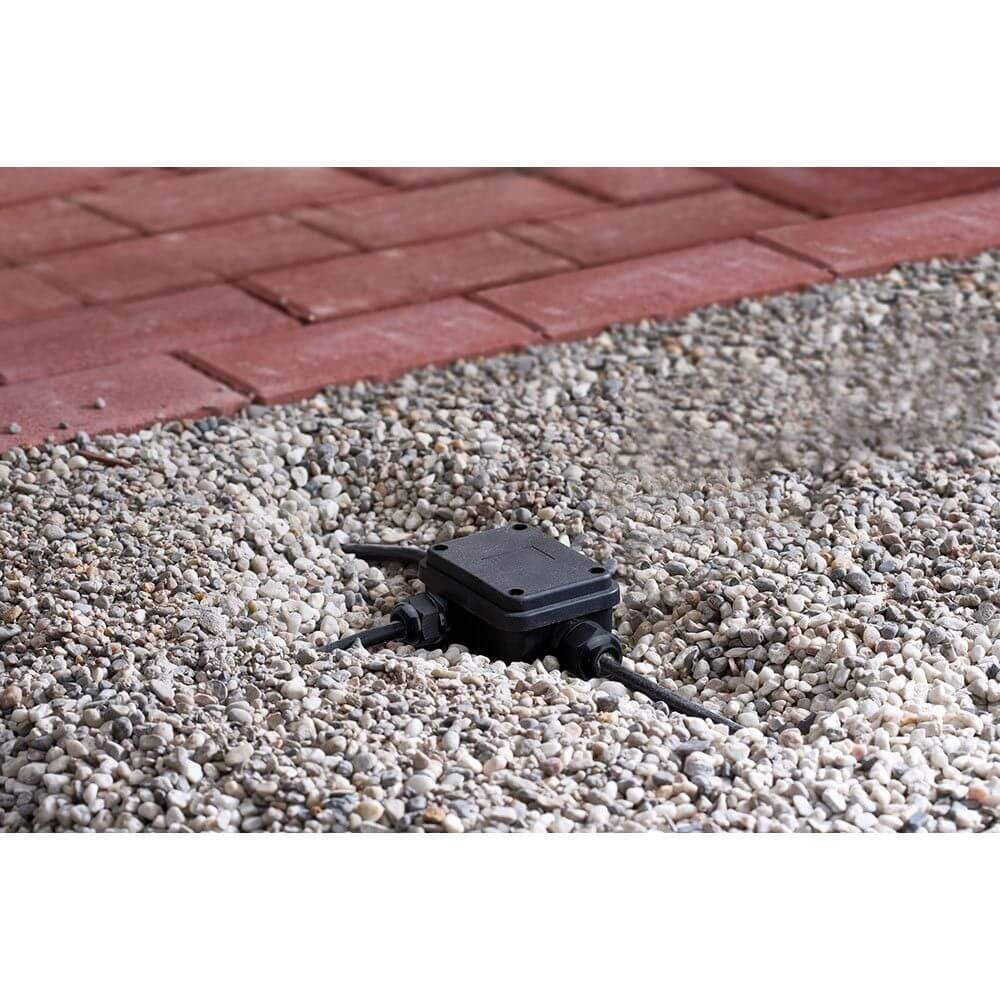 Verbindungsbox für Erdkabel 3-fach schwarz IP68 tauchwassergeschützt in Garteninstallation auf Kiesuntergrund.