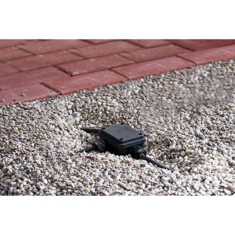 Verbindungsbox für Erdkabel 3-fach schwarz IP68 tauchwassergeschützt in Garteninstallation auf Kiesuntergrund.