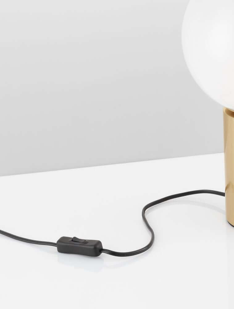 Nahaufnahme des Kabels mit Schalter einer Tischleuchte in Gold und Weiß auf einem Tisch.