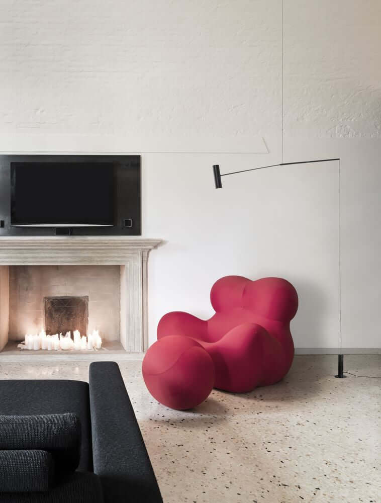 Gemütlicher Wohnraum mit rotem modernen Sessel, Kamin und schwarzem Sofa.