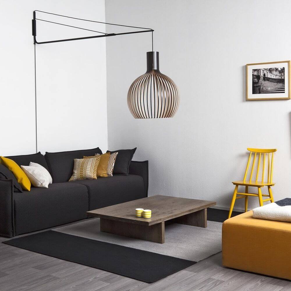 Wandhalterung Varsi 1000 für Pendelleuchten in modernem Wohnzimmer mit schwarzem Sofa und dekorativer Pendelleuchte.