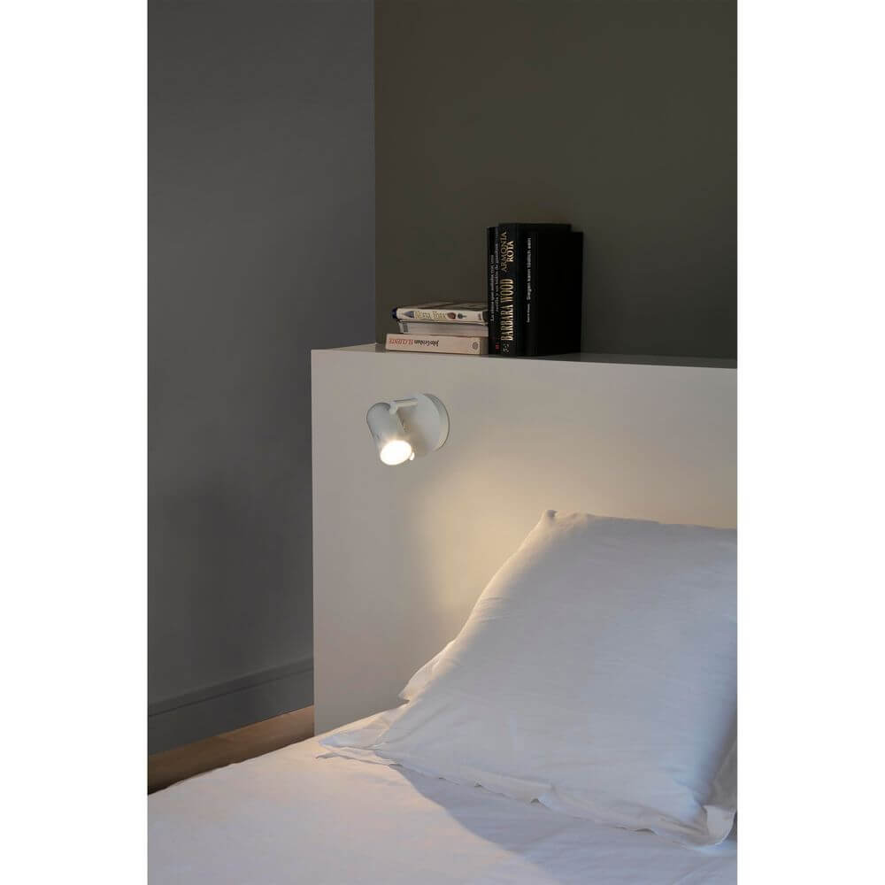 Spot Wandlampe ORLEANS Weiß an einem Bett mit weißer Bettwäsche und Nachttisch.