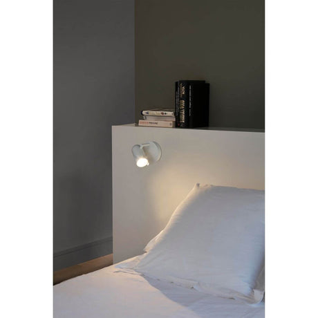 Spot Wandlampe ORLEANS Weiß an einem Bett mit weißer Bettwäsche und Nachttisch.