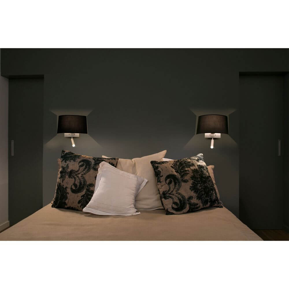 Wandlampe VOLTA mit LED-Leselicht 2700K Nickel, Schwarz neben einem Bett mit dekorativen Kissen.