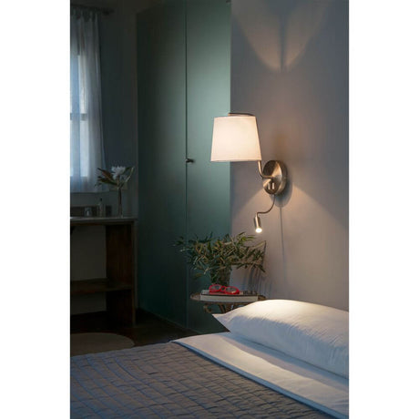 BERNI wall light with LED reading light, satin nickel in a cozy bedroom with bed and plants.