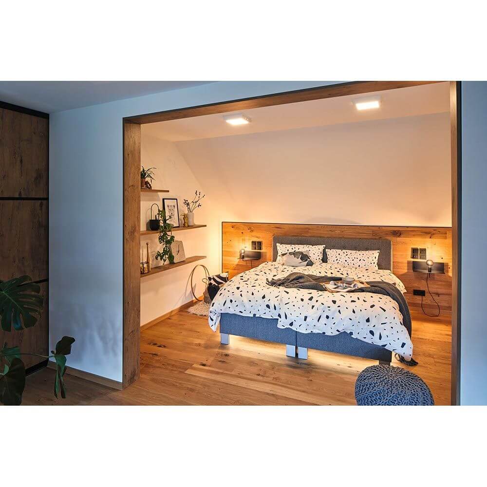 Schlafzimmer mit Wandleuchte Devara USB Schwarz neben Bett und stilvollem Holzregal.