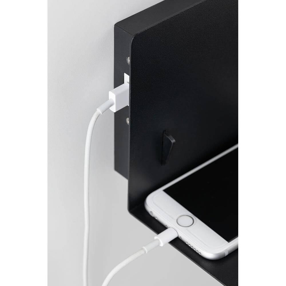 Wandleuchte Devara USB Schwarz mit integriertem USB-Anschluss und Smartphone auf der Ablage.