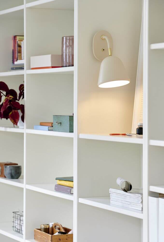 Wandleuchte Fleur 15 an einem Bücherregal, nostalgisches Design mit verstellbarem Lampenkopf in pudrigem Beige.