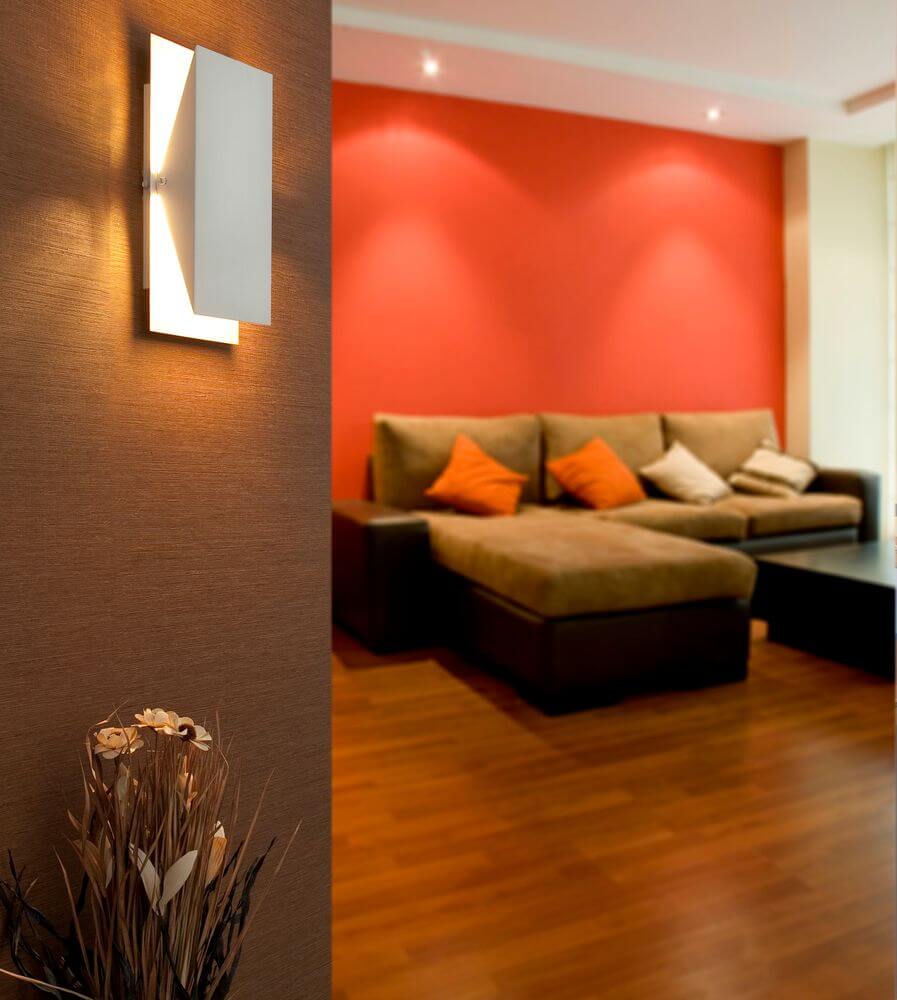Wandleuchte HOMS Weiß an einem modernen Wohnzimmer mit roter Wand und Sofa.