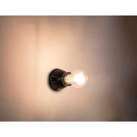 Wandleuchte KERA Schwarz an einer Wand mit einer leuchtenden Glühbirne.