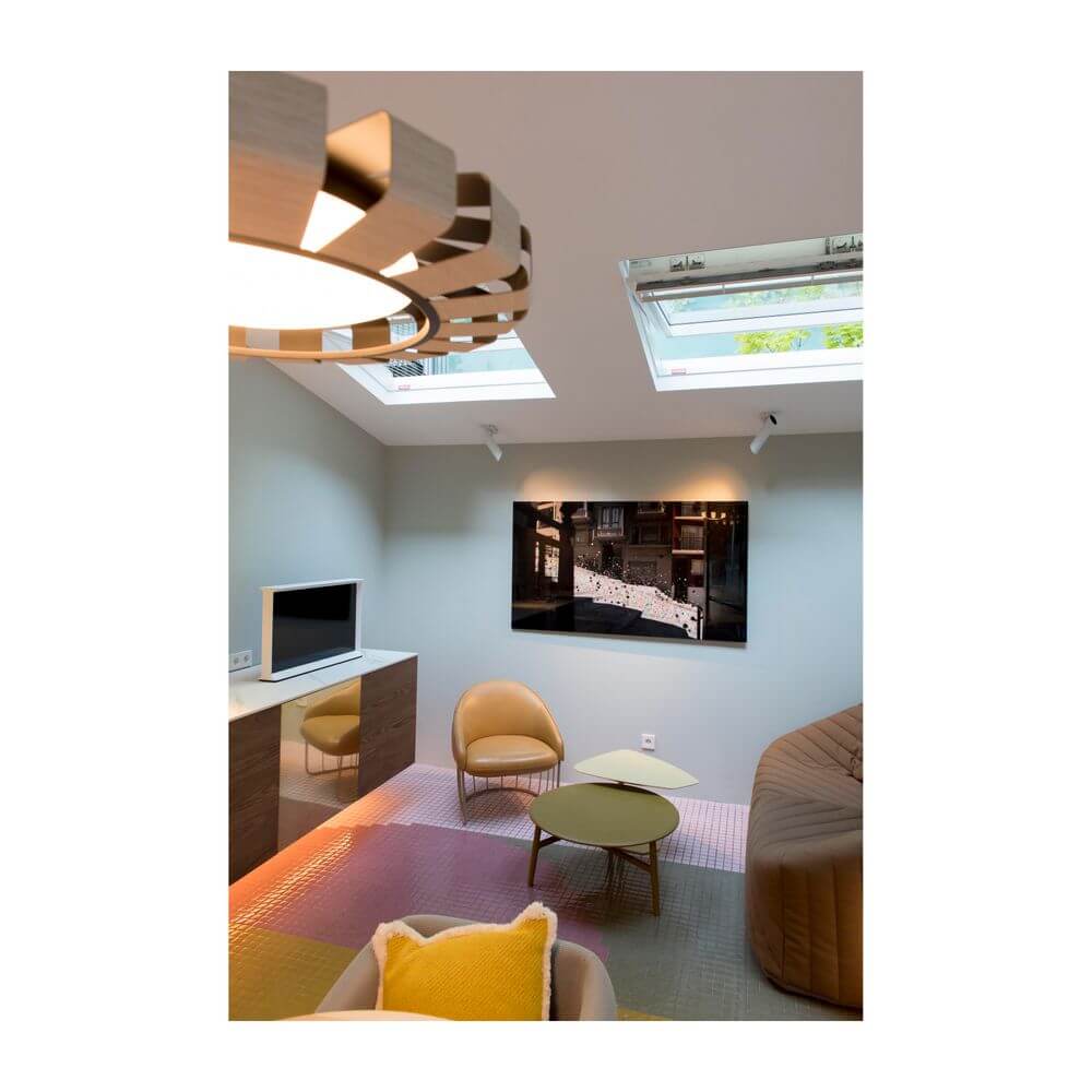 Moderne Wohnraum mit Wandleuchte LINK Weiß, Fernseher, gemütlichem Sessel und Tageslicht durch Dachfenster.