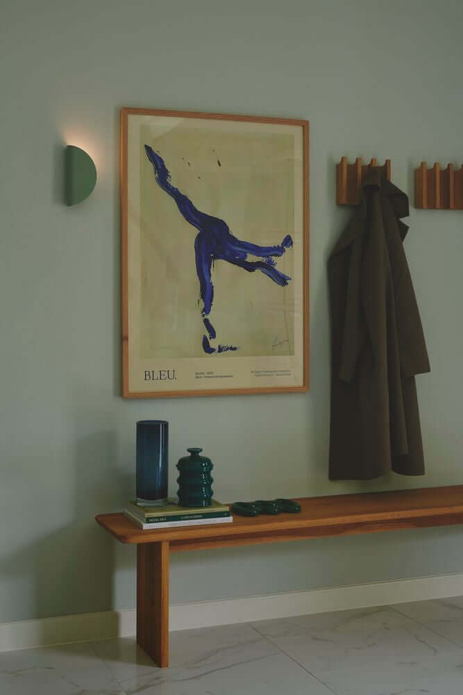 Moderne Wandleuchte Model 2110 an grauer Wand, dekoriert mit Kunst und Holzregal.