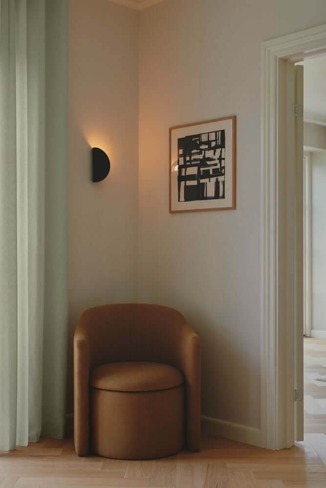 Wandleuchte Model 2110 an der Wand über einem beigen Sessel in einem modernen Raum.