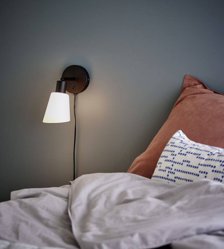 Wandleuchte Molli an der Wand über dem Bett, moderne Schlafzimmerbeleuchtung mit schwarzem Sockel und weißem Lampenschirm