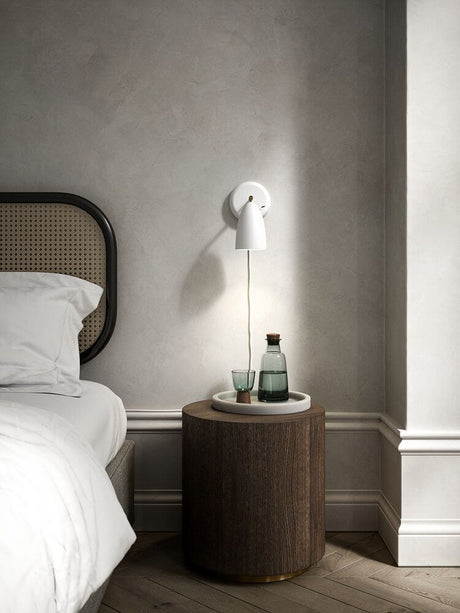 Wandleuchte Nexus 2 über einem Nachttisch mit Glasflasche und Gläsern, modernes nordisches Design.