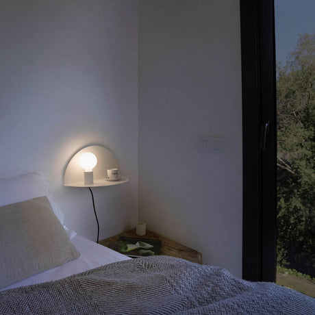 Vegglampe Nit hvit med avlastningshylle ved siden av en seng, koselig soveromsinnredning.