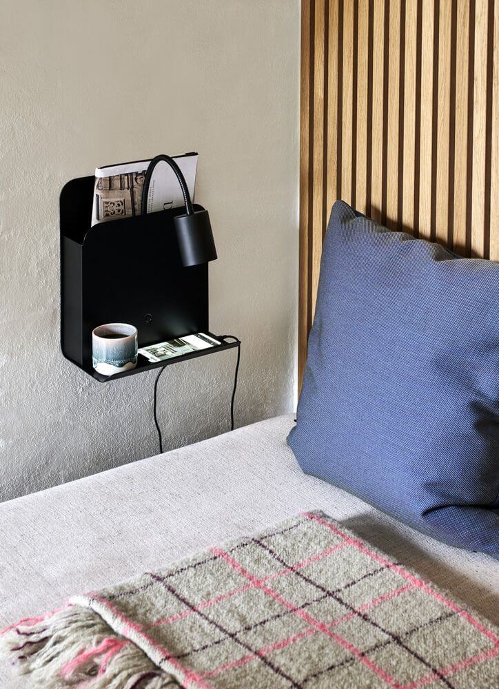 Wandleuchte Roomi an einer Wand montiert, kombiniert mit Ablage für Zeitschriften und Smartphone, stilvolles Wohnaccessoire.