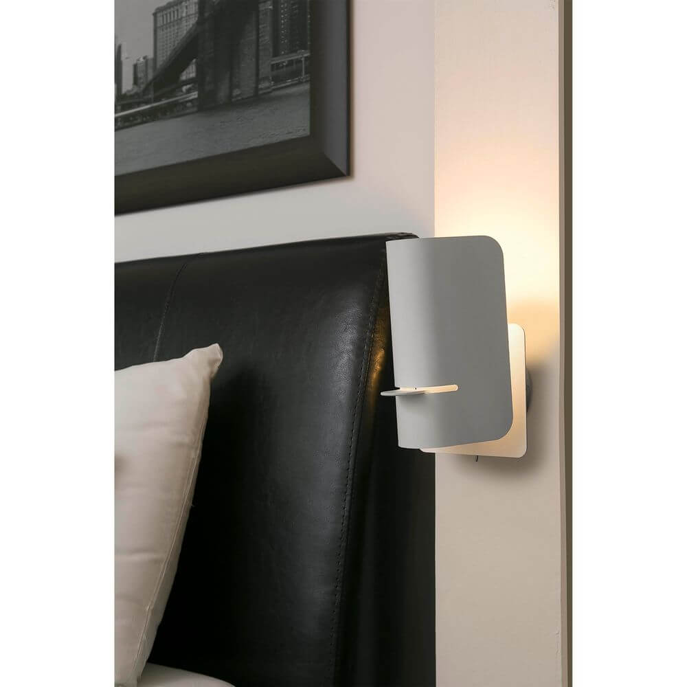 Wandleuchte SMILE Weiß an einer Wand neben einem Bett, bietet modernes Design und warmes Licht.