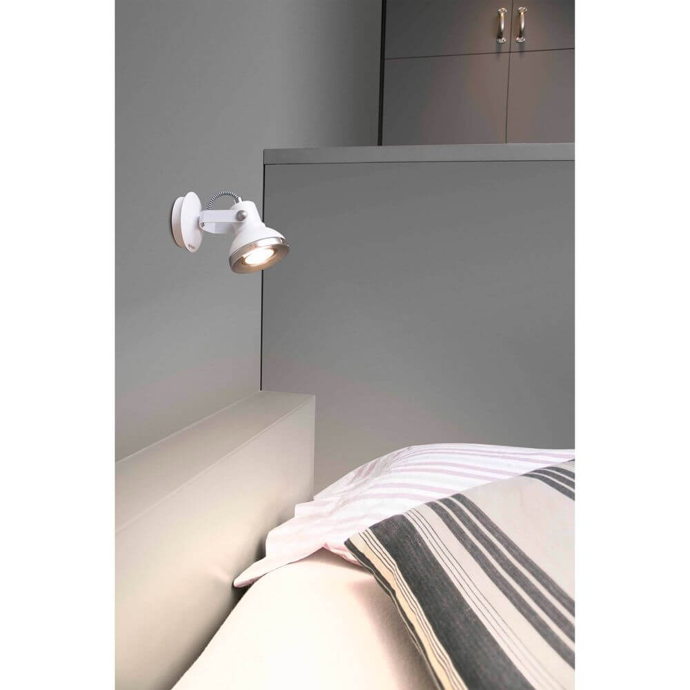 Wandstrahler RING-1 GU10 Weiß an der Wand neben einem Bett mit Kissen und Decke.