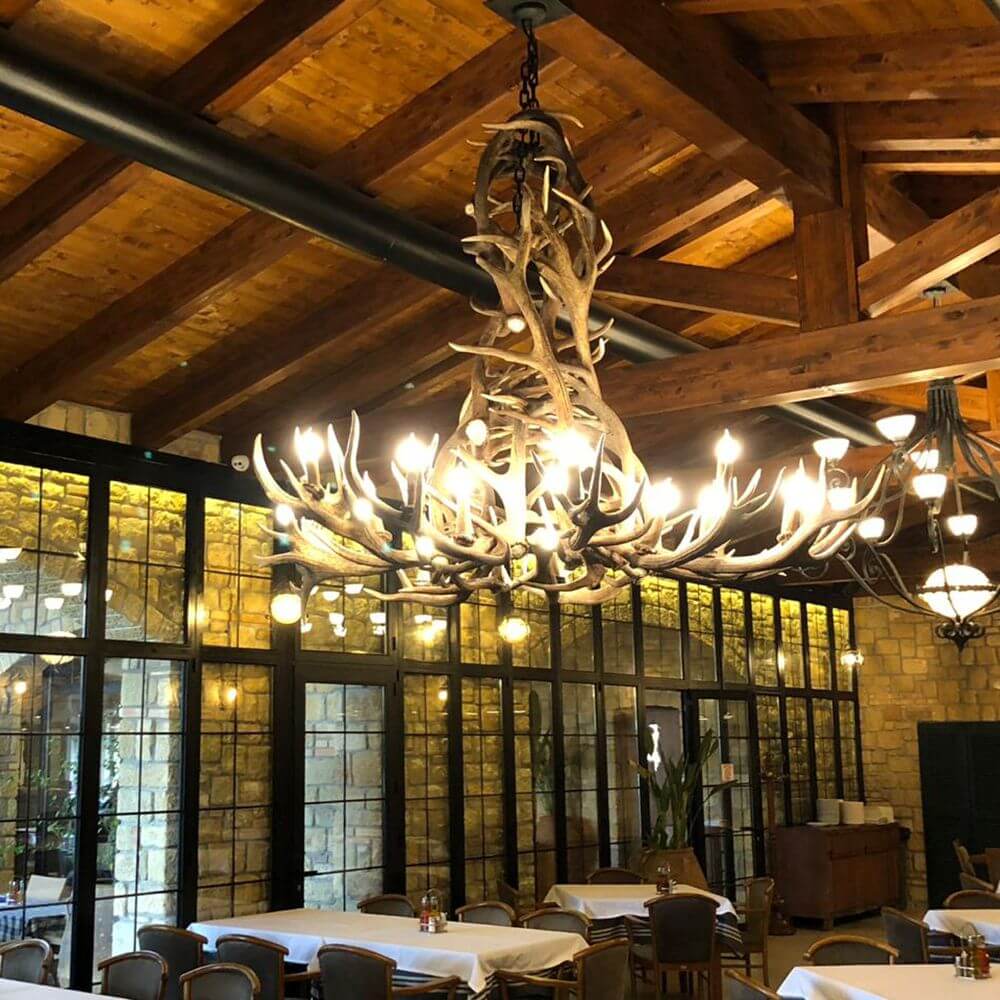 XXL Chalet Geweih Kronleuchter Ø 200cm im rustikalen Restaurant mit Holzdecke und Glaswänden.