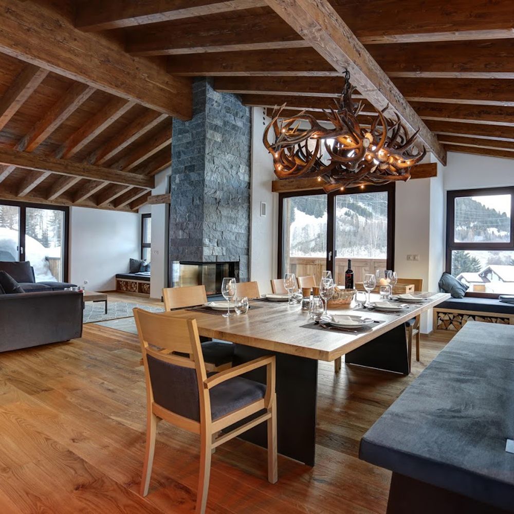 Chalet mit Holzdecken, Steinwand und XXL Rothirsch LED Geweihlampe im Essbereich zur stilvollen Beleuchtung.