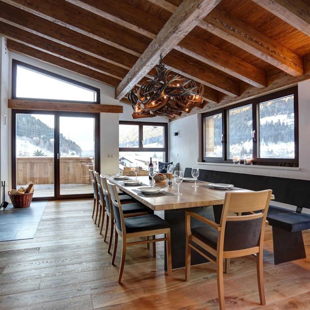 Modernes Esszimmer mit XXL Rothirsch LED Geweihlampe und Blick auf die Berge, ideal für Chalet-Atmosphäre.