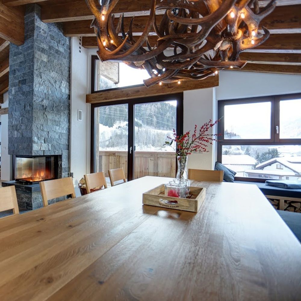 Rustikales Chalet mit XXL Rothirsch LED Geweihlampe über Eichenholztisch und moderner Steinkamin.