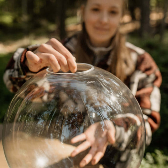 Ein junges Mädchen hält eine transparente Glaskugel in einem Wald, mit einem verschwommenen Hintergrund.