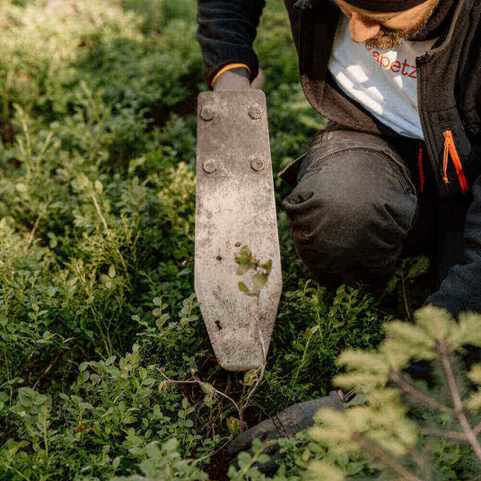 Ein Gärtner arbeitet im Garten mit einer Schaufel, um Pflanzen in der Erde zu bearbeiten.