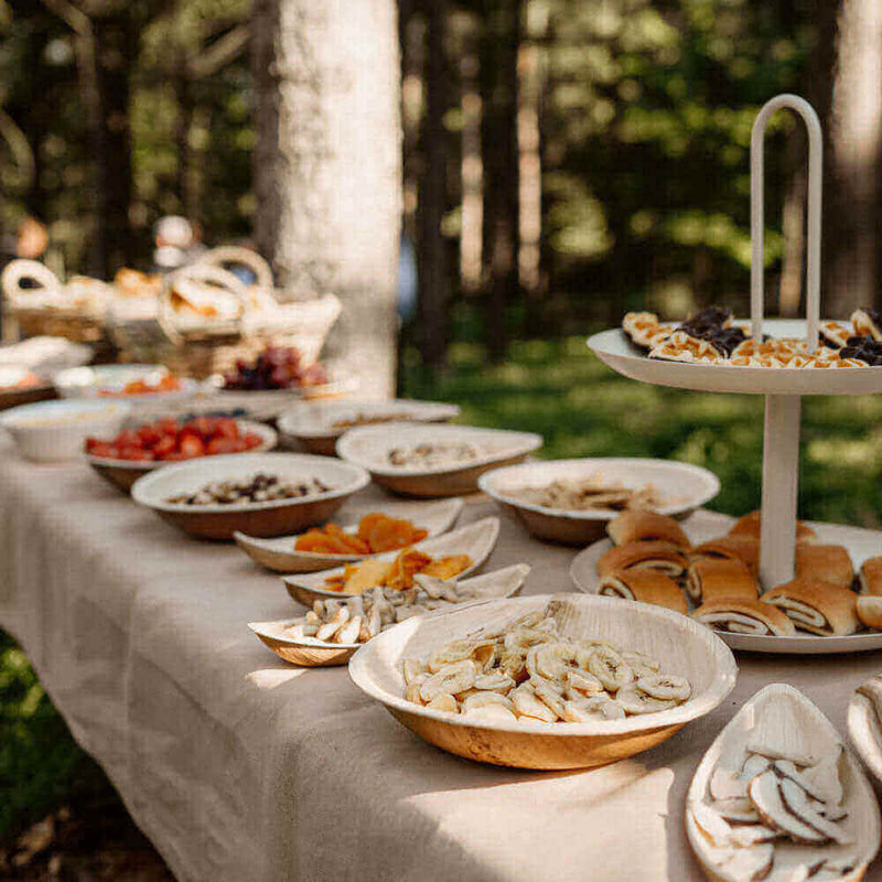 Beleuchtung s.luce, ein rustikales Buffet mit Obst und Snacks in einem Wald. Feine Holzschalen auf einem Tisch.