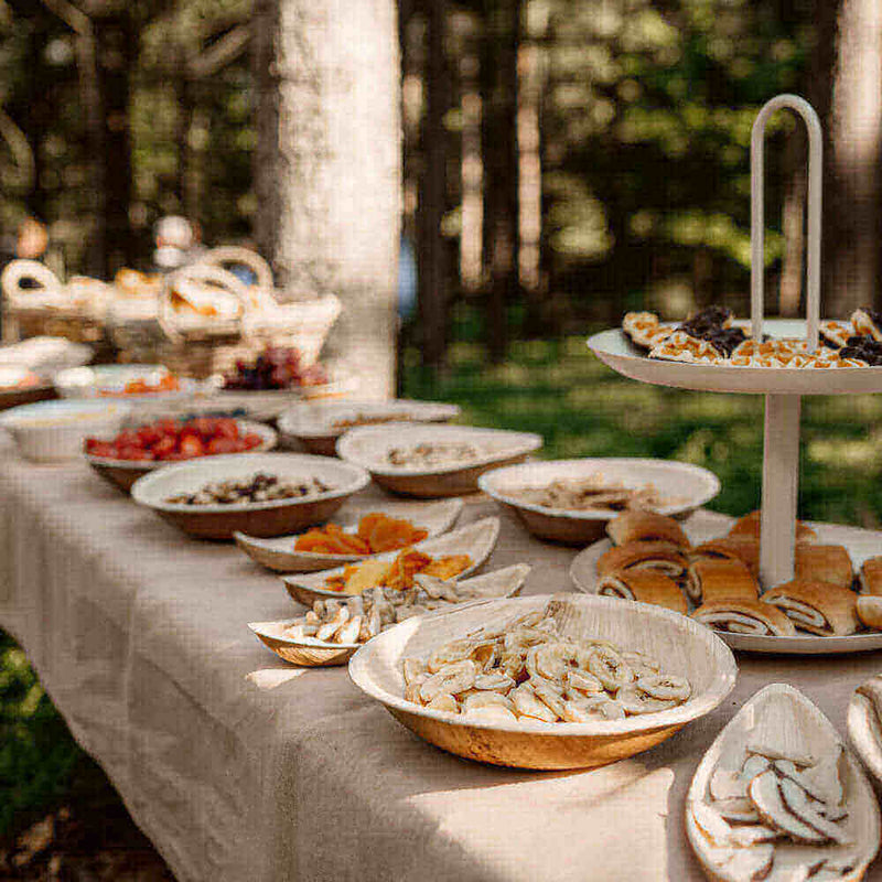 Beleuchtung s.luce, ein rustikales Buffet mit Obst und Snacks in einem Wald. Feine Holzschalen auf einem Tisch.