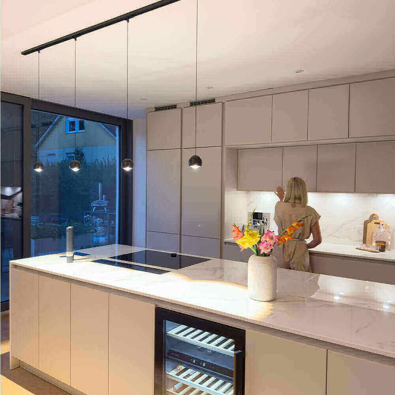 Moderne Küche mit eleganter Beleuchtung und einer Frau, die an der Arbeitsfläche arbeitet.