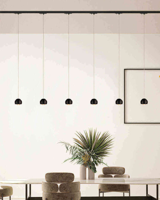 Moderne Deckenleuchten hängen über einem eleganten Tisch mit Pflanzen im Hintergrund.