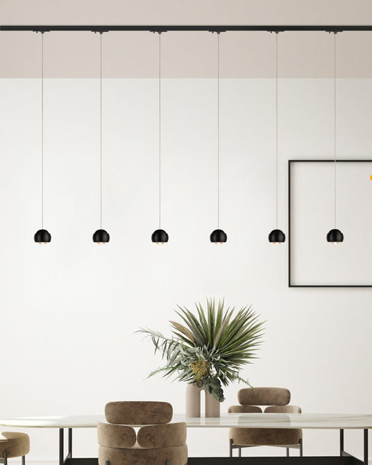 Moderne Deckenleuchten hängen über einem eleganten Tisch mit Pflanzen im Hintergrund.