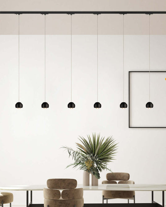 Moderne Deckenleuchten hängen über einem eleganten Tisch mit Pflanzen im Hintergrund.