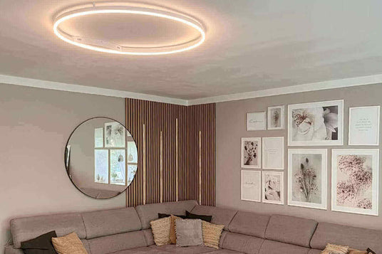 Moderne Wohnzimmeransicht mit runder Deckenleuchte, Spiegel und kreativen Wandbildern.