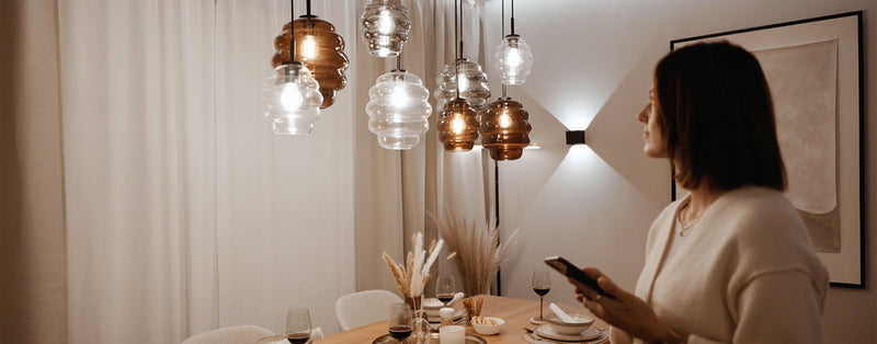 Frau in einem gemütlichen Esszimmer, die eine moderne Tischlampe bewundert, während sie ein Handy hält.