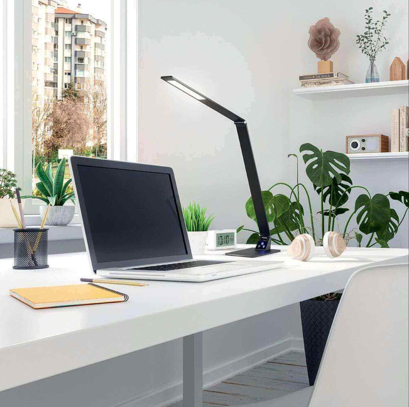 Helles modernes Home-Office mit Laptop, Schreibtischlampe und Pflanzen auf dem Tisch.